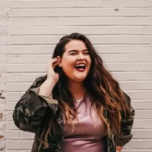 Mary-Burd-Grand-Forks-is-Cooler-Testimonial-WebP Woman laughing in front of a white brick building in Downtown Grand Forks