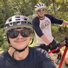 Biking in Grand Forks - State Parks WCT writer Paul and a friend wear sunglasses and a helmet as they smile and bike through a heavily wooded area.