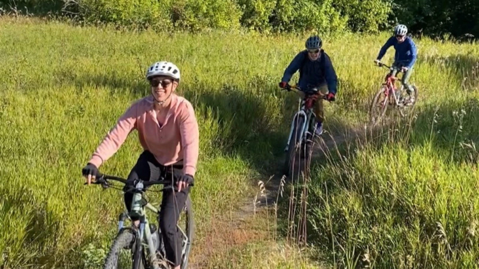 biking-grand-forks Three people ride their bikes in a line on a worn down, grassy trail.