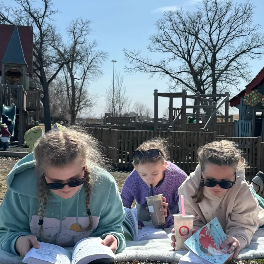 reading-park Three girls lay with Tea and Crepe beverages reading on a blanket in a Grand Forks park.