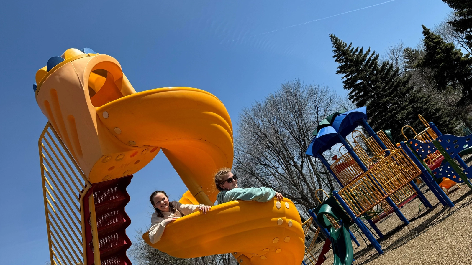 slide-park Two girls peak their heads over a yellow slide at a Grand Forks park.