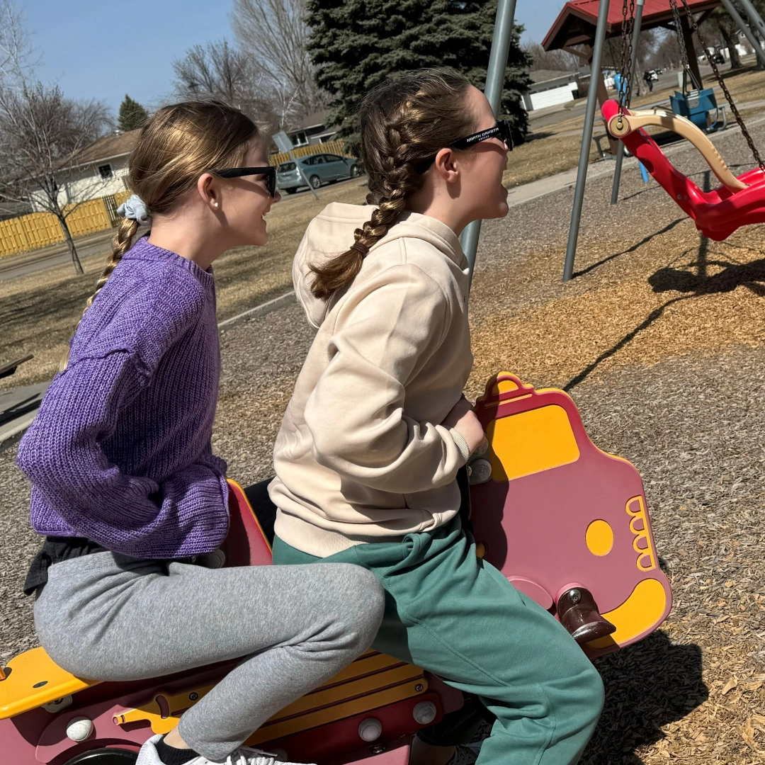 spring-riders Two girls sit on a spring rider at the park with swings in view.