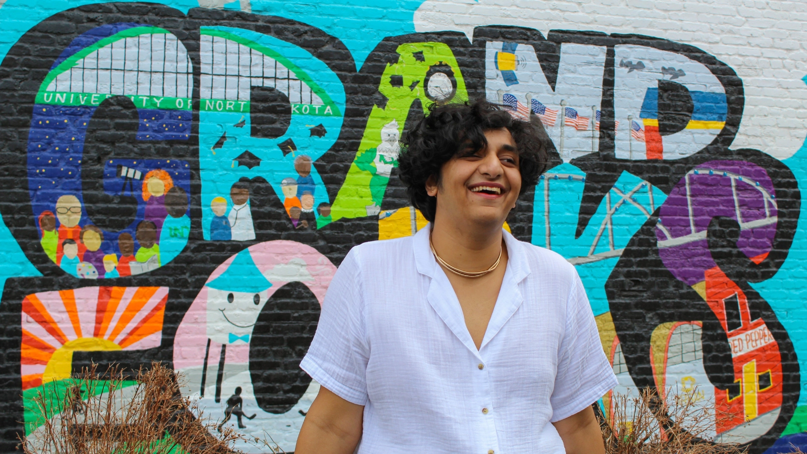 summer-in-grand-forks-jay 'What's Cooler Today?' Author Jay stands in front of Grand Forks art wall.