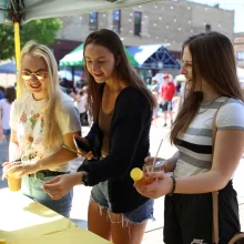 town-square-farmers-market-grand-forks-honey Three girls buying honey at Town Square Farmer's Market in Grand Forks.