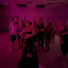 Grand Forks Glow Up Body WCT author Isabelle takes a mirror selfie with nine other members of her workout class. The room is lit red and everyone is dressed in workout attire.
