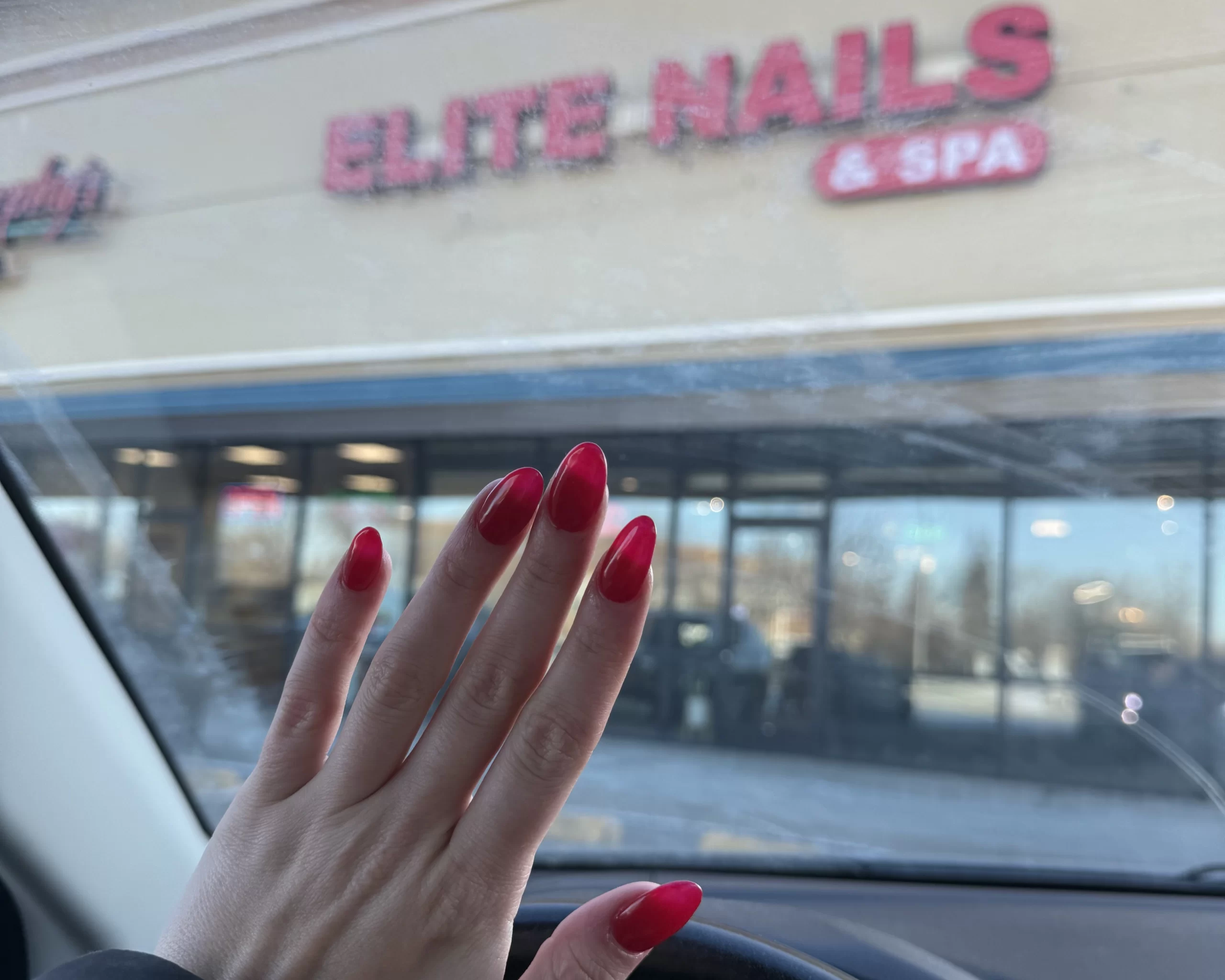 Grand Forks Glow Up Nails WCT author Isabelle flaunts her new red manicure in front of a nail salon storefront that reads "Elite Nails & Spa"