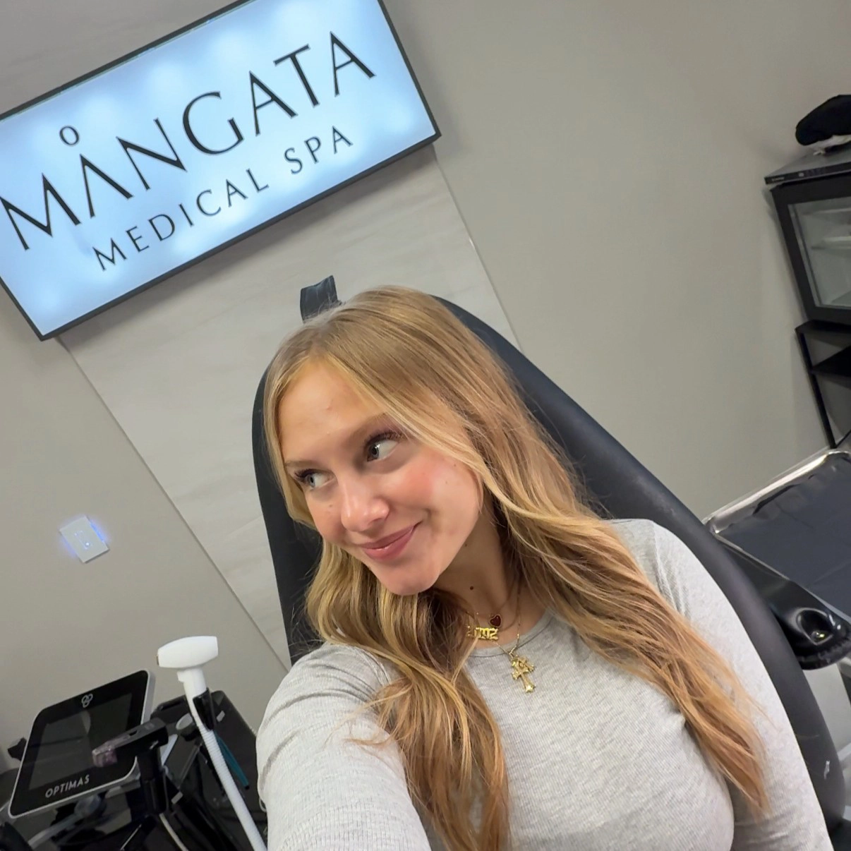 Grand Forks Glow Up Skin WCT author Isabelle takes a selfie in a chair with a sign behind her that reads "Mangata Medical Spa"