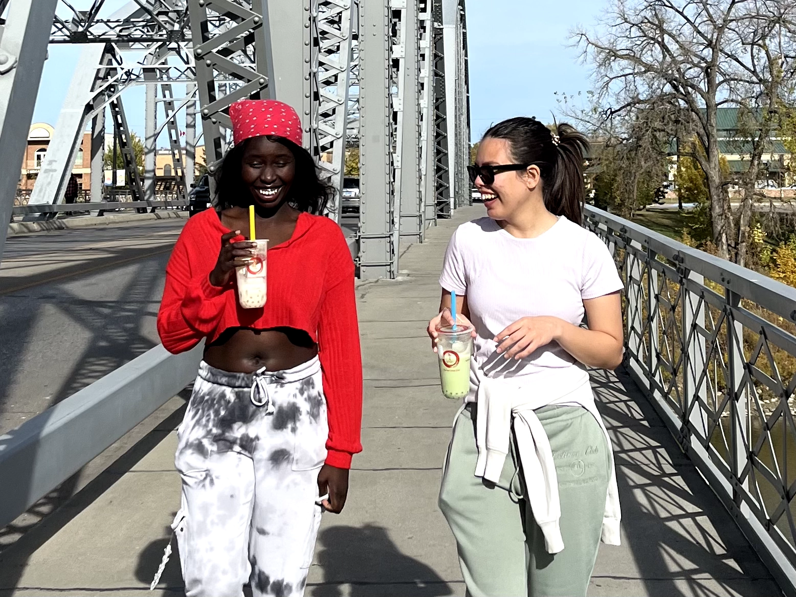 Tea-and-crepe-grand-forks Two girls walking across the bridge in Grand Forks with teas from Tea & Crepe
