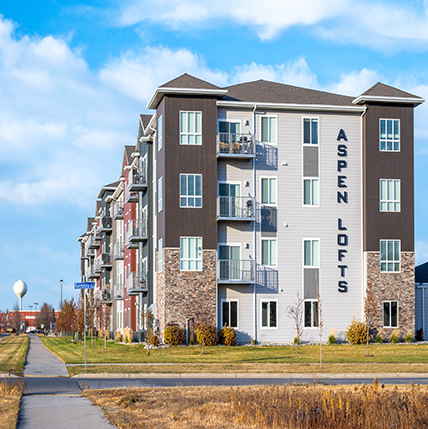 Aspen Lofts - Exterior APPROVED Aspen Lofts Apartments. A big complex with shades of beige and brown siding. Lots of windows and balconies showing.