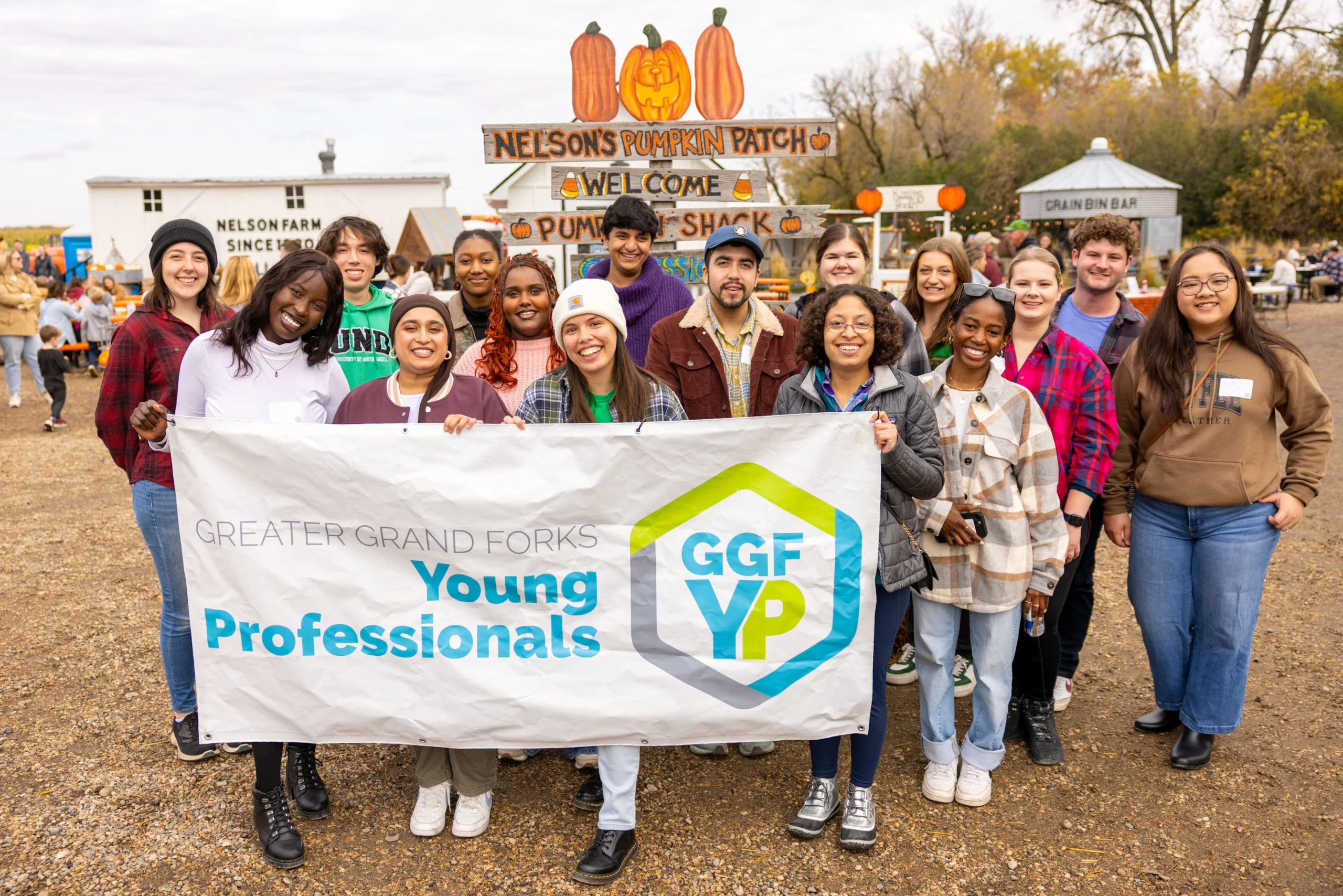 Nelson's Pumpkin Patch group photo Author Gon Carlson stands in the middle front of a large group of young professionals at Nelson's Pumpkin Patch. They hold the GGFYP logo banner.