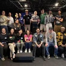 Mario Cart League GGFYP group photo A large group of young professionals sit for a photo after their Mario Cart League event. They are in an indoor venue.
