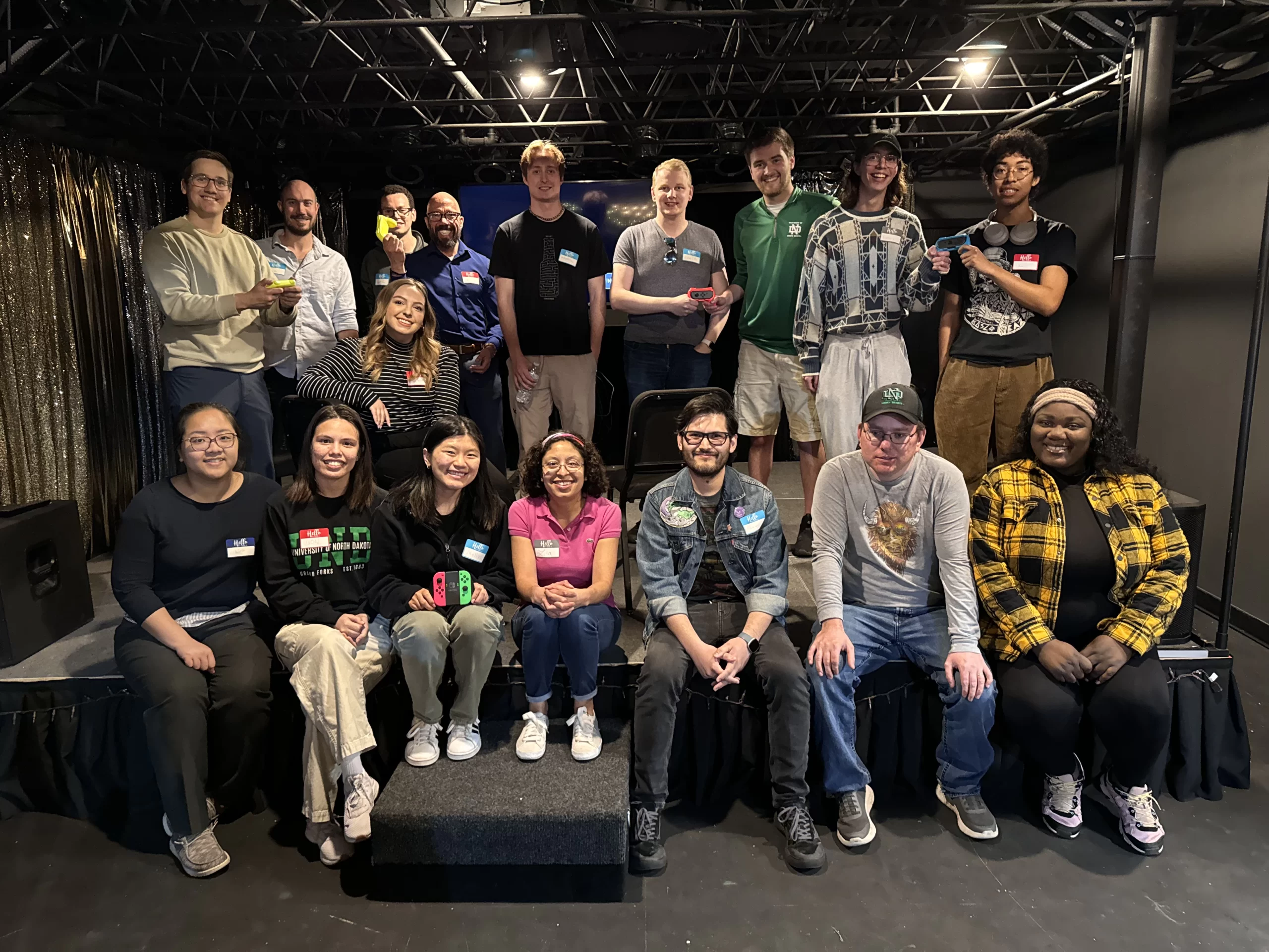 Mario Cart League GGFYP group photo A large group of young professionals sit for a photo after their Mario Cart League event. They are in an indoor venue.
