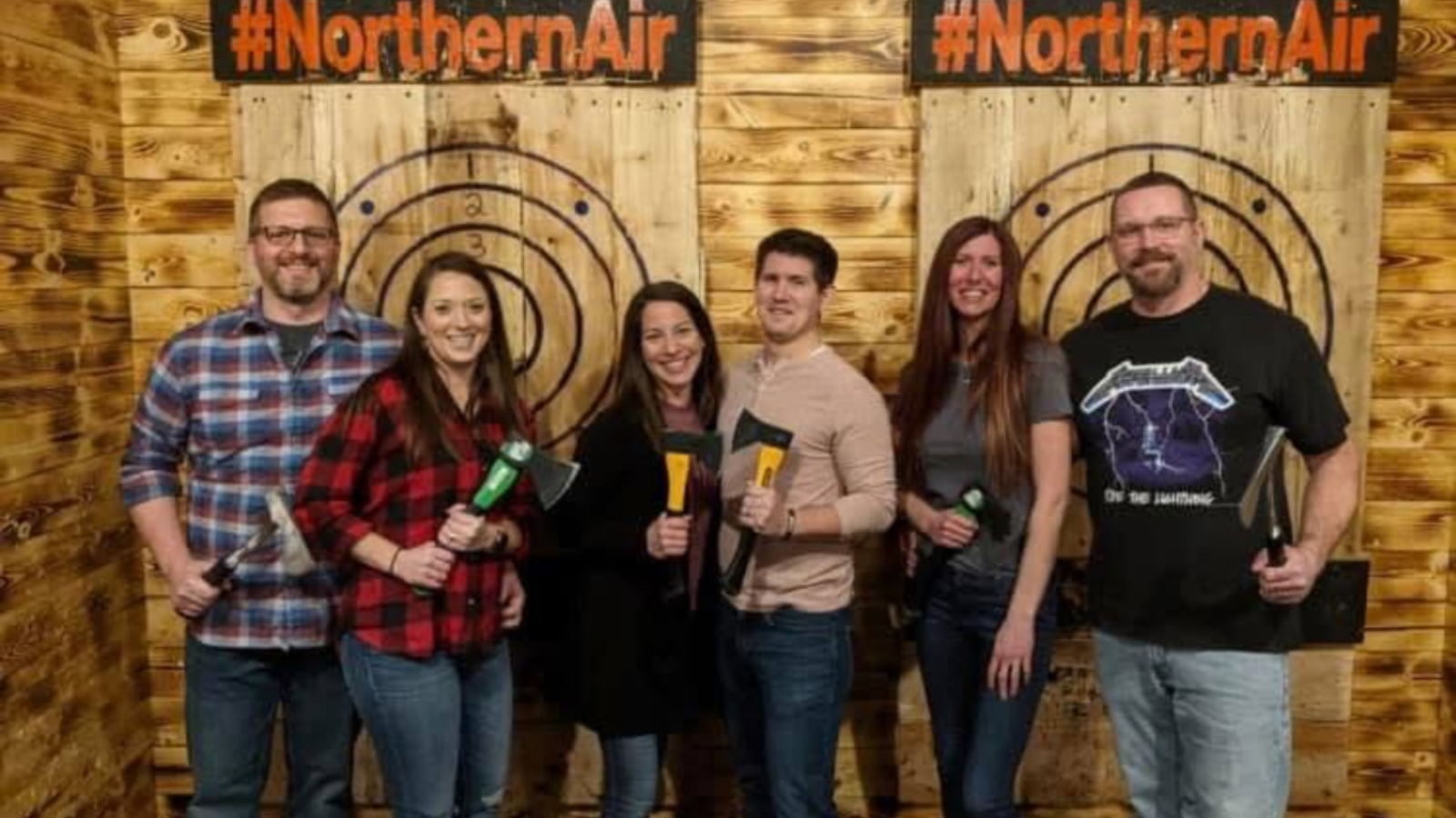 Author Bry stands in the middle of freinds as they are at the Northern Air Axe Throwing. They stand in front of the targets smiling with their axes.