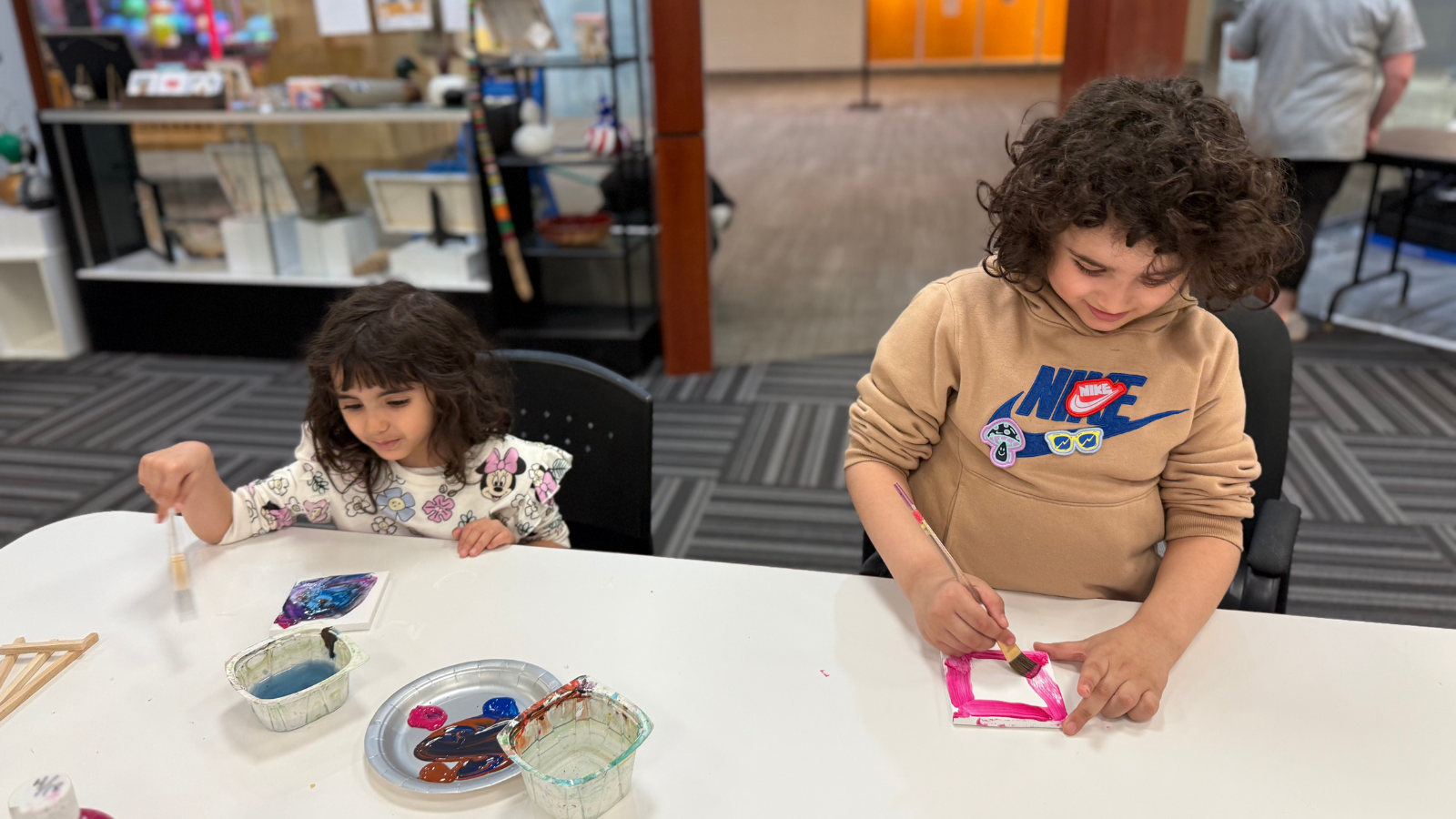 Crafting Kiddos Photo Kiddos work on their artful creations in this photo. They sit at a crafting table with all their supplies laid out in front of them.