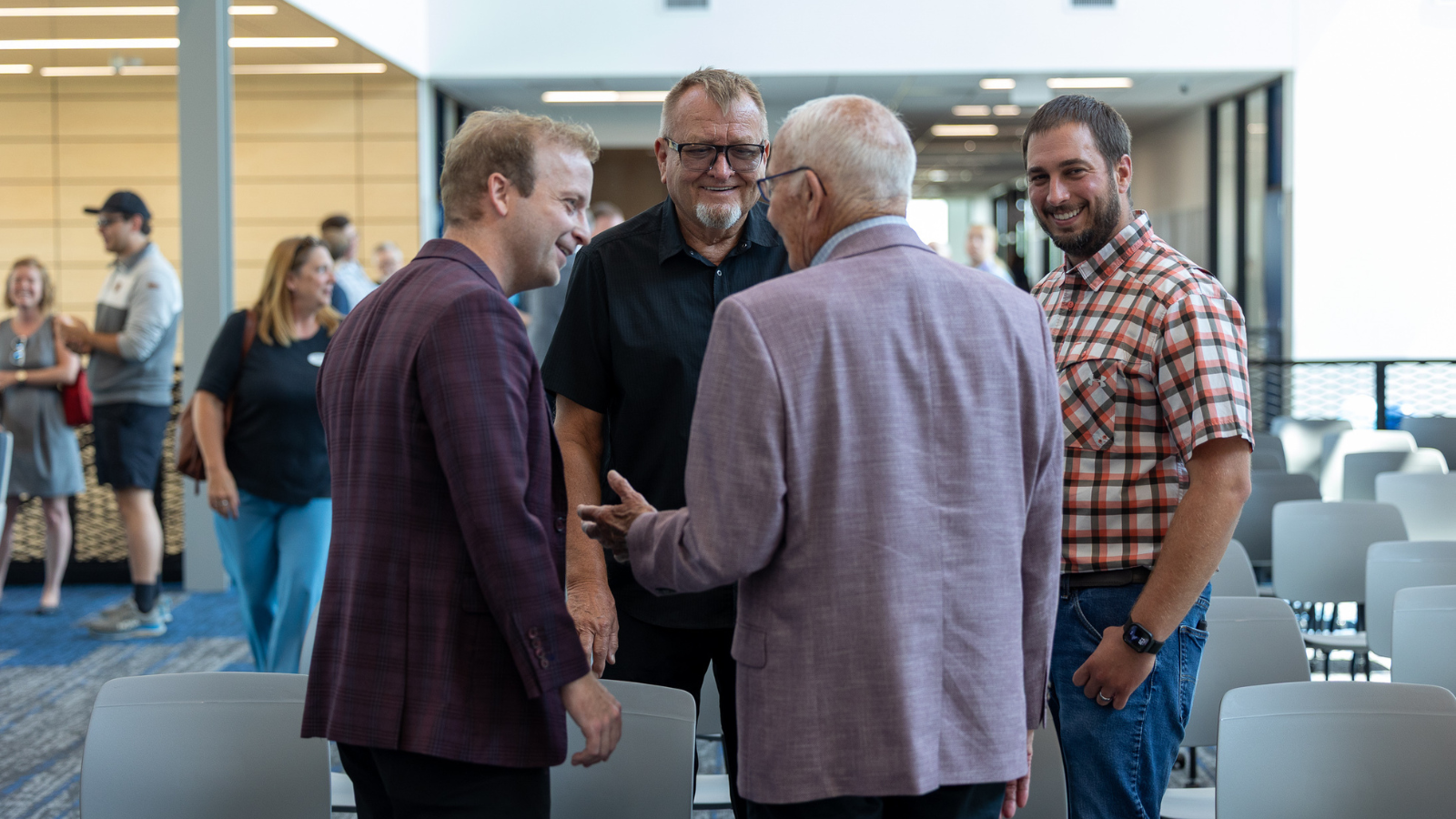 Business Conversations with Smiles at CIA A group of businessmen in varying outfits talk with smiles during the grand opening of the Grand Forks Career Impact Academy