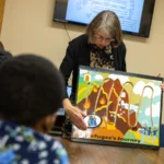 Featured image shows a representative from Global Friends Coalition showing a group of volunteers the refugee's journey via a diagram.