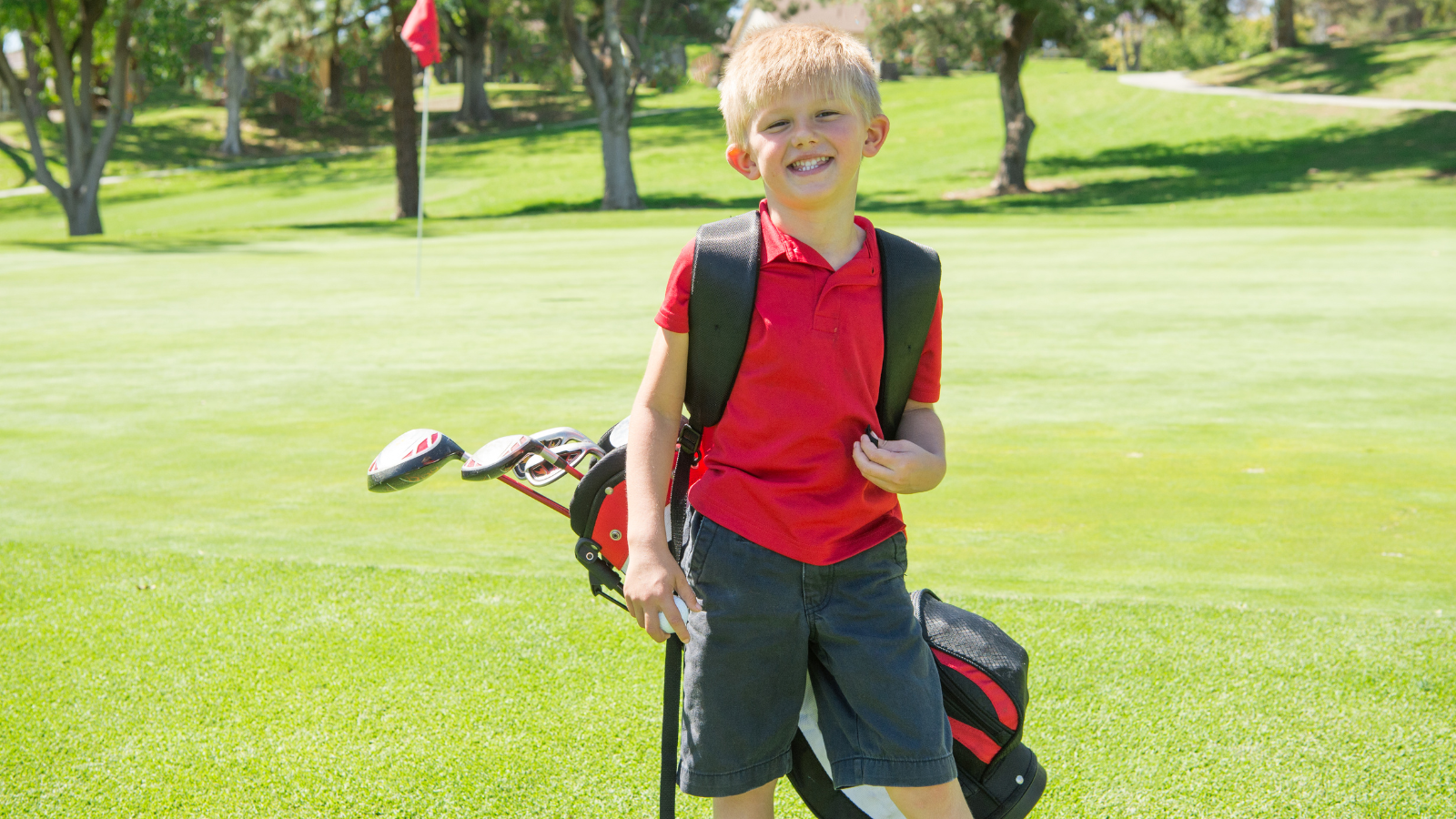 Young boy smiles at the camera while holding golf clubs on the course