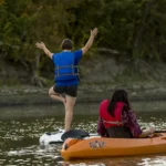 A kayaker and paddle boarder along the Red River take a minute to pause so the paddle boarder strikes a yoga pose on the board