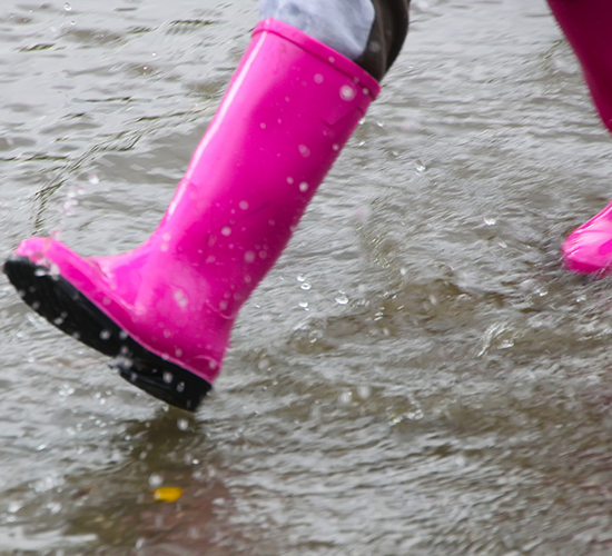 A pink rain boot stomps through the puddles on a rainy day in Grand Forks